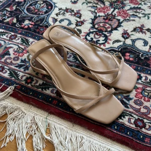 Beige sandaler med klack från H&M - Snygga beige sandaler från H&M med smala remmar och fyrkantig tå. Skorna har en stabil blockklack och är gjorda i syntetmaterial. Perfekta för dig som gillar minimalistisk och trendig stil.