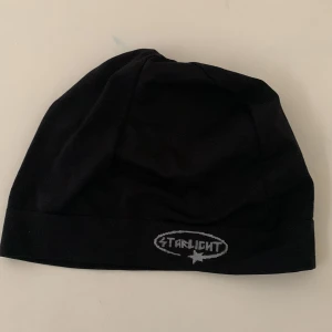 Svart mössa Starlight logga - Svart mössa från Starlight med en grå logga framtill. Enkel och stilren design, perfekt för kalla dagar. Tillverkad i mjukt material som sitter skönt på huvudet. Passar dig som gillar en clean look med en touch av street.