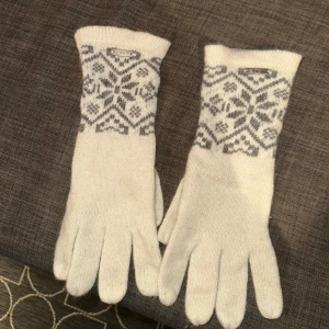 Ull vantar  - Stickade handskar i vitt med grått snöflingemönster. Långa muddar och klassisk nordisk design, perfekta för kalla dagar. 70% ull, mjukt och varmt material som känns skönt mot huden.