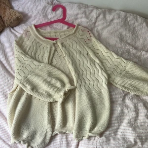 Söt ljusbeige stickad kofta - Superfin ljusbeige stickad kofta med vågigt hålmönster och volangdetaljer vid ärmslut och nederkant. Koftan har en enkel knäppning upptill och ballongärmar som ger en chill och trendig vibe. Perfekt att slänga över en topp när det är lite kyligt ute. Stirleken står inte men skulle gissa på ungefär xs och passar mig som har allt från xxs till S. 