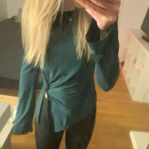 Grön långärmad omlottblus - Snygg grön långärmad blus med omlottdetalj och knyt i sidan. Modellen har en avslappnad passform och är perfekt för dig som gillar stilrena plagg med en twist. Tyget ser mjukt och skönt ut, och färgen är riktigt fräsch.