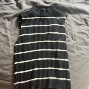 Randig ribbad ärmlös topp Gina Tricot - Snygg svart ribbad ärmlös topp från Gina Tricot i storlek XS. Toppen har vita horisontella ränder och en hög krage som ger en cool vibe. Perfekt att styla med jeans eller kjol för en trendig look.