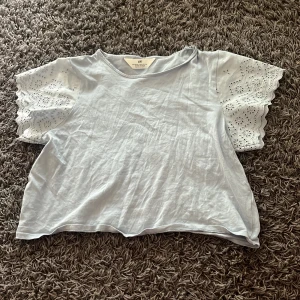 Ljusblå topp med broderade ärmar H&M - Supersöt ljusblå topp från H&M med korta, broderade ärmar och vågig kant. Ärmarna har hålbroderier i blommönster.  Skriv till mig privat om ni vill ha en bättre bild.