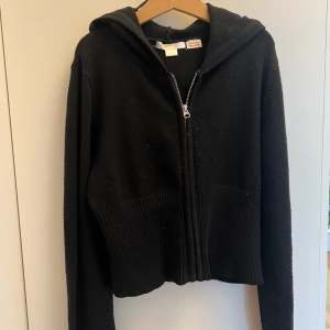 Svart stickad hoodie - Svart catania liknande hoodie från Gina tricot  med hel dragkedja framtill och huva. Tröjan har ribbade detaljer vid midjan och är tillverkad i ett mjukt, stickat material. Perfekt för lager-på-lager och chill dagar.
