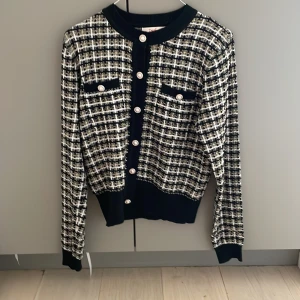 Rutig kofta från Derhy med guldknappar - Snygg rutig kofta från Derhy i svart, vitt och inslag av guld. Koftan har långa ärmar, dekorativa guldknappar framtill och vid fickorna samt ribbade muddar. Perfekt för dig som vill ha en chic och trendig look med lite extra detaljer. Den är i väldigt bra skick men har några trådar som hänger ut (de kan man alternativt klippa bort). Denna tröja passar personer som är mellan 170-175 cm. Jag är 174 och den passar fint. Den är storlek M. 