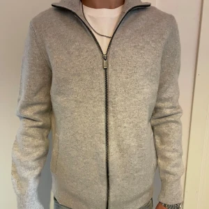 Ljusgrå kofta från Massimo Dutti - Snygg ljusgrå kofta från Massimo Dutti i en blandning av ull och kashmir. Jackan har hel dragkedja framtill, ribbade muddar och hög krage. Perfekt för dig som gillar en clean och stilren look. Nypris 3500 pris kan diskuteras vid snabba köp.