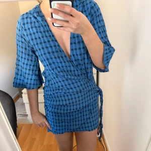  Zara Blå rutig omlottklänning 🩷 - Snygg blå kort omlottklänning med svart rutigt mönster och trekvartsärmar. Klänningen har v-ringning och knyt i sidan för en smickrande passform. Perfekt för dig som gillar en trendig och avslappnad stil. 💖