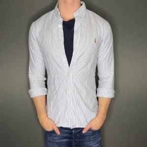 Blårandig Ralph lauren skjorta - Hej säljer nu min fina Ralph lauren skjorta i storlek M. Den är i bra skick men har ett pytte litet hål på baksidan men knapp syns och kommer vara otroligt snygg nu i vår och framåt sommaren. Nypris cirka 1600kr! Vi kommer att sälja liknande produkter nu i vår och närmare sommar så glöm inte följa profilen!🌊🍾