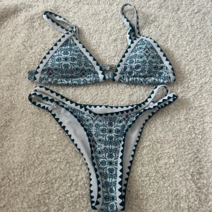 Blåvit mönstrad bikini med triangel - Snygg bikini med blått och vitt mönster. Överdelen har triangelformade kupor och smala axelband, underdelen är högt skuren med samma mönster. Båda delarna har dekorativa kanter i mörkblått och vitt. Perfekt för stranden eller poolen! Aldrig använd, endast testad!