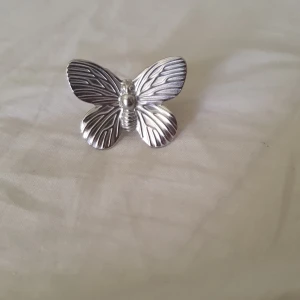 Silvrig ring med fjäril - Cool ring i silverfärgad metall med en stor, detaljerad fjäril på ovansidan. Fjärilen har markerade vingar med snygga linjer och ringen är justerbar för att passa olika storlekar. Perfekt statement piece för dig som gillar unika accessoarer.