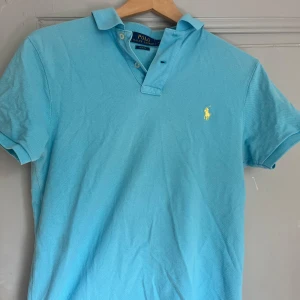 Ljusblå pikétröja från Ralph Lauren - Snygg ljusblå pikétröja från Ralph Lauren i slim fit-modell.  Tillverkad i bomull, fräsch o skön till sommaren .