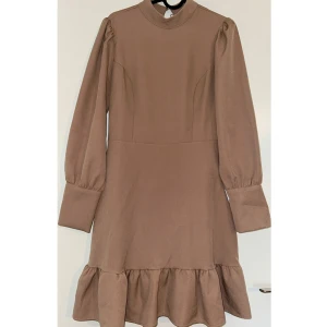 Beige volangklänning från Trendyol - Supersöt beige kortklänning från Trendyol med volangkant nertill, höga manschetter med knappar och puffiga långärmar. Klänningen har hög hals och en snygg söm som markerar midjan. Perfekt för dig som gillar en stilren look med en twist.