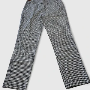 Svartvita mönstrade kostymbyxor - Snygga svartvita kostymbyxor med grafiskt mönster från SFERA spanskt varumärke . Byxorna har rak passform och är tillverkade i bomull med lite stretch för extra komfort. Perfekta för dig som vill sticka ut med en cool och modern look. Mått: Midja 34cm Höfter 42 Inre benlängd 59cm.