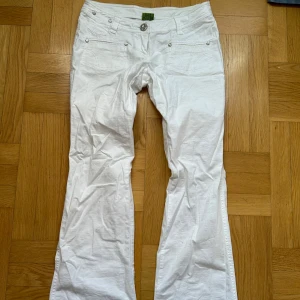 Y2K, Lågmidjade, utsvängda, vita byxor från Refree - Det Lågmidjade vita byxor med vida ben i bottnen. Helt rena, knappt använda. Med tryck & jättegulliga knappar. Y2K, Vintage style! Strl: S L74  W73,5 🌷 Snygga vita byxor från Refree i bootcut-modell med silverfärgade knappar och detaljer. Byxorna har normal passform, mycketbra tillstånd och är tillverkade i ett lätt bomullsmaterial. Perfekta för dig som gillar en fräsch och stilren look.