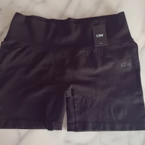 Svarta träningstights shorts från ICANIWILL - Svarta, högmidjade träningstights shorts från ICANIWILL med diskret logga på benet. Stretchigt material i syntet, perfekt för gym eller löpning. Baksidan har snygg rynkdetalj som framhäver formen. Sitter tight och bekvämt med bred midjeresår.