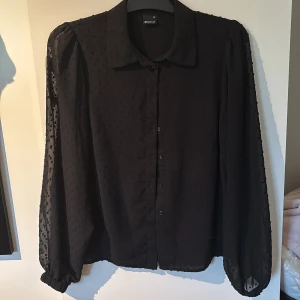 Svart prickig skjorta - Svart skjorta från Gina Tricot i storlek 36. Fin detalj med prickar i tyget. Knäppning framtill. Långa, lätt transparenta ärmar med resår vid ärmslut ger en snygg och luftig känsla. Köparen står för frakt.
