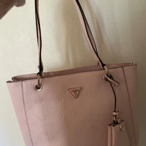 Ny Guess rosa väska  - Säljer en ljusrosa axelväska från Guess med präglat mönster och guldfärgade detaljer. Helt oanvänd. Köpt för 1890kr. Priset kan diskuteras