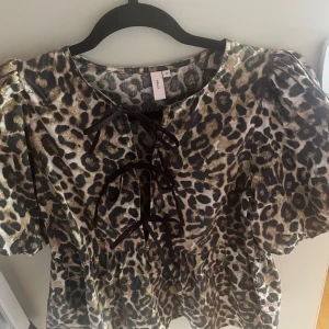 Leopardmönstrad topp från Nelly - Snygg topp från Nelly med leopardmönster i bruna och svarta toner. Klänningen har puffiga korta ärmar och snörning framtill vid halsen. Perfekt för dig som vill sticka ut med en trendig look. Har bara provat.
