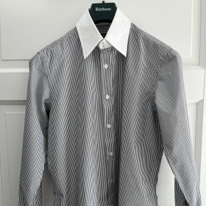 Randig skjorta från BOSS med vit krage - Snygg skjorta från BOSS med smala svarta och vita ränder och en kontrasterande vit, bred krage. Skjortan har klassisk knappstängning och långa ärmar. Perfekt för dig som vill sticka ut med en stilren och modern look.