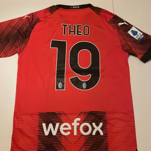 AC Milan Theo 19 matchtröja Puma - AC Milan hemmatröja replika säsong 2023/2024 med Theo och nummer 19 på ryggen. Röd bas med svarta grafiska mönster, officiella Serie A-märke på ärmen och klubbmärke på bröstet. Tillverkad i lätt funktionsmaterial, klassisk V-ringning och korta ärmar. Endast handtvätt gäller!