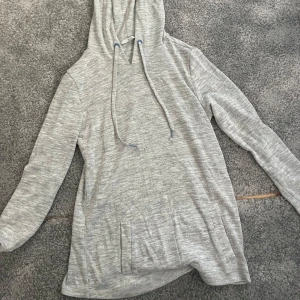 Ljusgrå hoodie från ASOS - En stilren ljusgrå hoodie från ASOS med långa ärmar, huva och snörning. Tröjan har en normal passform och är tillverkad i mjuk bomullsmix. Perfekt för chill dagar eller när du vill ha en enkel och clean look.