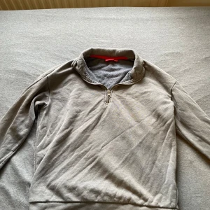 Grå half zip tröja från RYVLS - Mysig grå tröja från RYVLS med halv dragkedja och hög krage. Tillverkad i mjuk bomullsmix med fleece på insidan för extra komfort. Perfekt för kyliga dagar och enkel att matcha med jeans eller mjukisbyxor.
