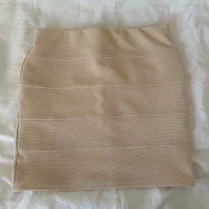 Beige tight kjol från Tally Weijl - Säljer en beige, tight kjol från Tally Weijl i kort modell. Kjolen har en stilren design med horisontella sömmar och är gjord i ett stretchigt material som sitter snyggt på kroppen. Perfekt för dig som gillar en enkel men trendig look