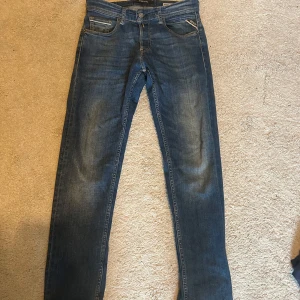 Blå Replay jeans Anbass 28/32 - Säljer ett par snygga Replay Anbass jeans i klassisk blå tvätt. Jeansen har fem fickor, raka ben. Märkespatch bak på linningen och coola detaljer på bakfickorna. Perfekta för dig som gillar en stilren look.