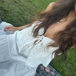 Vit broderad topp med knytning - Superfin vit topp med broderade blommor och knyt framtill. Lätt och luftig med ärmlös design, perfekt för varma dagar. Söt och passar till många olika outfits nu i sommar.