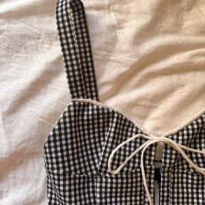 Rutig korsettopp från Zara - Supersnygg eftertraktat svartvit rutig korsettopp från Zara med breda axelband och söt knytning framtill. Toppen har hakknäppning och markerade sömmar för en figurnära passform. Perfekt att styla med jeans eller kjol för en trendig look. 🌸