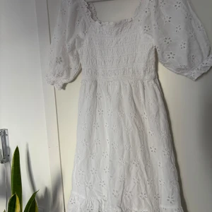 Vit broderad sommarklänning XS - Superfin vit klänning med broderade blommor, puffärmar och smockad överdel. Klänningen har en romantisk vibe med volangkant nertill och är perfekt för varma dagar. Tillverkad i bomull och har en luftig passform.