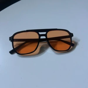 Svarta pilotbågar med orange glas - Snygga solglasögon med svart pilotbåge och orangefärgade glas. 