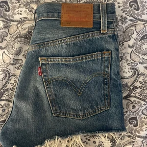 Levi's jeansshorts med fransig kant - Snygga blå jeansshorts från Levi's med klassisk femficksdesign, låg midja och rå, fransig kant nertill. Ikonisk läderpatch bak och röda Levi's-tag på bakfickan. Perfekta för sommardagar och ger en avslappnad vibe.