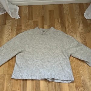 Beige stickad tröja med rund hals - En enkel och stilren beige stickad tröja med rund halsringning och ribbade muddar. Tröjan har en rak passform och är långärmad, perfekt för lager-på-lager under kyliga dagar.