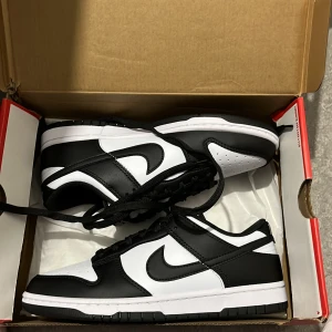 Nike Dunk Low svart/vit sneakers - Nike Dunk Low sneakers i klassisk svart och vit färg. Skorna har en låg silhuett, svart snörning och vit perforerad tå.   Storlek 41 Eu. Helt oanvända 