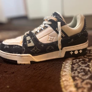 Louis Vuitton sneakers svart/vit - Snygga Louis Vuitton sneakers i svart och vitt med klassiskt monogrammönster. Skorna har rund tå, snörning och detaljer i skinn och textil. Tjock sula med LV-logga undertill och coola kontraster mellan svart och vitt. Perfekta för dig som vill sticka ut med lyxig streetstyle.