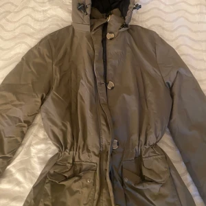 Olivgrön parkajacka från NLY Trend - Snygg olivgrön parkajacka från NLY Trend med huva, stora fickor och knappar framtill. Jackan har dragsko i midjan för en schysst passform och är perfekt för kyligare dagar. Stängs med både dragkedja och knappar. Enkel och stilren design.