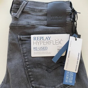 Replay Hyperflex Anbass grå jeans 31/32 - Snygga Replay Hyperflex Anbass jeans i grått med klassisk femficksdesign. Jeansen är tillverkade i en mix av bomull och återvunnen polyester för extra stretch och komfort. Aldrig använda