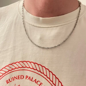 Tunn silverfärgad kedja halsband - Säljer ett stilrent halsband med tunn, tvinnad kedja i silverfärg. Perfekt för dig som gillar minimalistiska smycken och vill ha något som funkar till alla outfits. Lätt att matcha med andra accessoarer. Osäker på märke. Helt nytt 