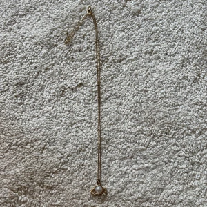 Guldigt halsband med pärlhänge - Snyggt halsband i guld med ett unikt hänge som liknar en planet med en vit pärla i mitten. Kedjan är tunn och elegant, perfekt för att ge din outfit en cool touch. Passar dig som gillar trendiga och stilrena smycken. OBS!!!! KOMMER GÖRAS RENT INNAN SICKAD