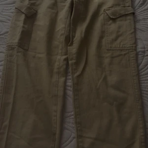 Khaki cargopants med fickor - Säljer ett par khaki cargopants med stora fickor på sidorna. Byxorna har en avslappnad passform och är perfekta. Materialet känns slitstarkt och de har klassiska cargodetaljer.