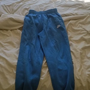 Blå mjukisbyxor från Nike  - Säljer ett par blå mjukisbyxor från Nike i storlek M. Byxorna har resår i midjan, sidofickor och en broderad Nike-logga i vitt på låret. Perfekta för chill dagar eller träning. Mjukt material som känns skönt mot huden. Köpte dem på en nike butik i barcelona för 500kr, knappt använda, säljer nu för 250 för halva pris