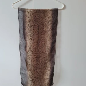 Leopardmönstrad tunn halsduk/scharf - Säljer en snygg och tunn halsduk/scharf med leopardmönster i bruna och svarta nyanser. Halsduken är rektangulär och har en lätt och luftig känsla. Mått: 150x33 cm.