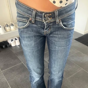 Lågmidjade bootcut jeans från Lee - Säljer ett par snygga blå jeans från Lee med låg midja och bootcut-ben. Jeansen har slitna detaljer, dubbla knappar i midjan och klassiska fickor fram och bak. Storlek W27 L31, skriv för frågor och prisförslag! Kan gå ner i pris mycket!💗