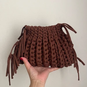 Brun handgjord stickad handväska - Unik handväska i chunky stickad design, gjord av mjukt brunt bomullsgarn. Väskan har coola knytband i hörnen som ger en bohemisk vibe. Perfekt storlek för det viktigaste och riktigt snygg accessoar till din outfit.