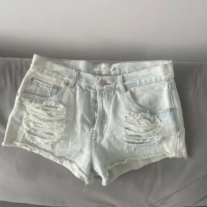 Ljusblå ripped jeansshorts - Snygga ljusblå jeansshorts från bikbok med slitna detaljer och råa kanter. Klassisk femficksmodell med hög midja och dragkedja. Perfekta för varma dagar och ger en avslappnad vibe.