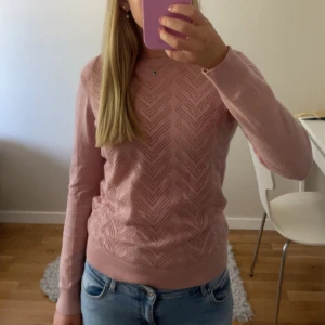 Ljusrosa stickad tröja från Bondelid - Supersöt ljusrosa stickad tröja från Bondelid i storlek XS. Tröjan har ett snyggt hålmönster i zigzag på framsidan och långa ärmar. Mjuk och skön kvalitet, perfekt till jeans eller kjol. Liten Bondelid-logga på ena ärmen för extra detalj.