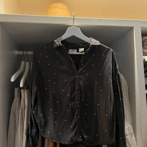Svart prickig skjorta från Levi's XS - Svart kortare skjorta från Levi's i storlek XS med små gula prickar över hela tyget. Skjortan har klassisk krage, knappar framtill och långa ärmar. Materialet är mjukt och har en lätt glansig finish, vilket ger en cool och modern vibe.