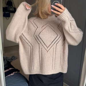 Beige stickad tröja med mönster - Säljer en beige stickad tröja med snygga hålmönster i geometriska former. Tröjan har en loose passform, långärmade ärmar och hög hals. 