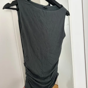 Mörkgrå ärmlös topp från Gina Tricot - Snygg topp från Gina med snygga detaljer på sidan som ser väldigt fint ut på! Mörk grå/grön färg som passar bra med både silver och guld smycken. Pris går att diskutera,storlek xs. 